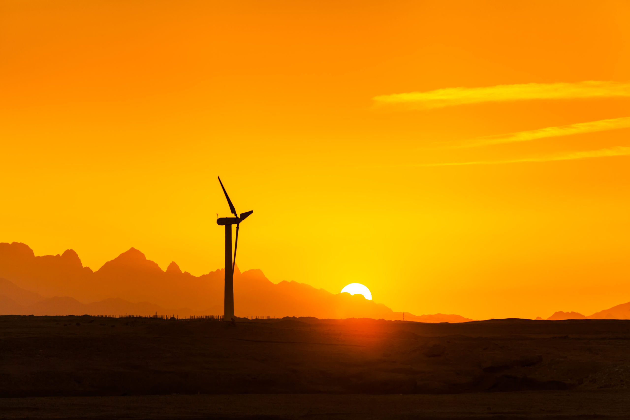 Big wind turbines in the desert against mountains.