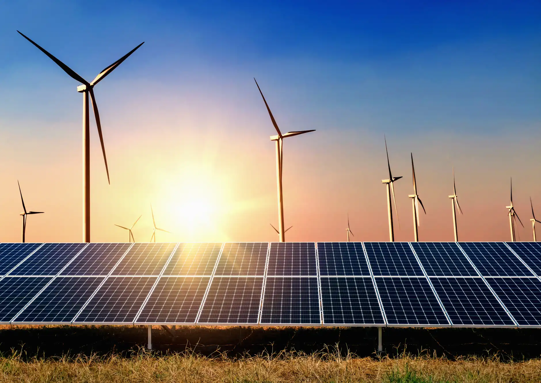 Photo of the sun setting behind wind turbines and solar panels.